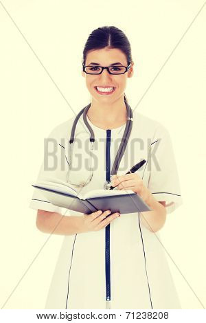Young female doctor wirting in a book. Isolated on white.