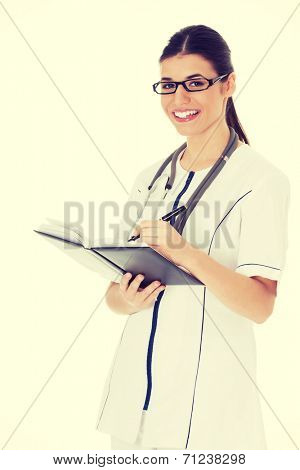 Young female doctor wirting in a book. Isolated on white.