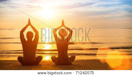 Yoga silhouette of a young couple on the beach at sunset.