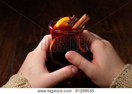 Man's Hands Hold A Glass With Mulled Wine, Mulled Wine With An Orange, Honey, Cinnamon, A Carnation