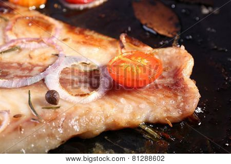 Dish of Pangasius fillet with onion and cherry tomatoes on burn pan background