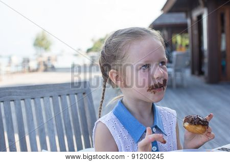 Adorable little girl having breakfast eating chocolate donut at outdoor cafe