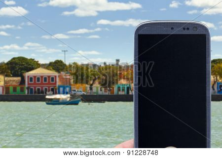Smatrphone and a landscape. Idea for travel apps, digital detox, taking shots, accessing apps, Internet, blogs and others. The blur image are Colored houses at Porto Seguro coast - Bahia - Brazil