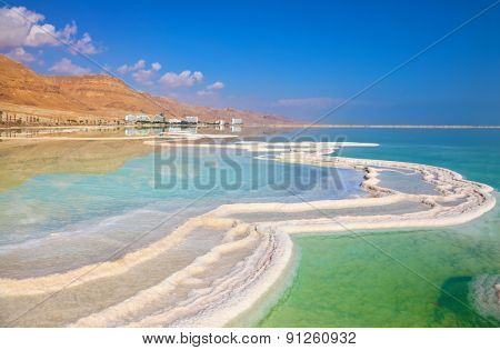Israeli coast of the Dead Sea. The path from salt picturesquely curls in salty water. Hotels are reflected in smooth water ashore