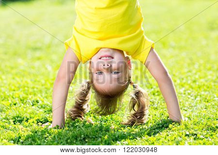 kid girl standing upside down on her head on grass in summer
