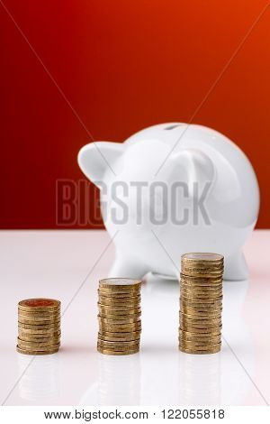 White piggy bank with a stack of coins and a red background
