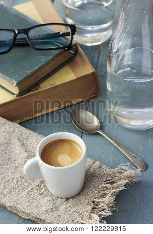 Espresso with water on blue wooden table, with books in the background