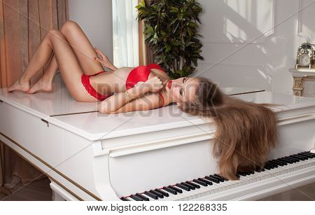 studio glamour photo of female model lying in red lingerie on piano