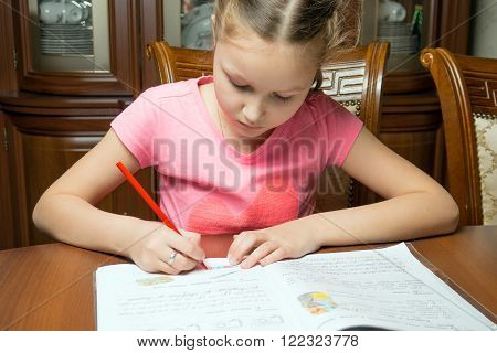 Girl doing homework. She writes in a notebook at the table.