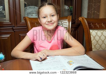Girl doing homework. She writes in a notebook at the table.