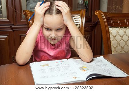 Girl doing homework. She writes in a notebook at the table.