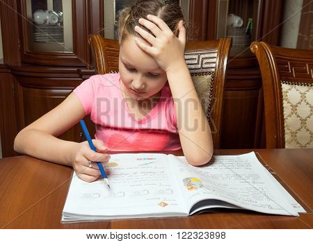 Girl doing homework. She writes in a notebook at the table.