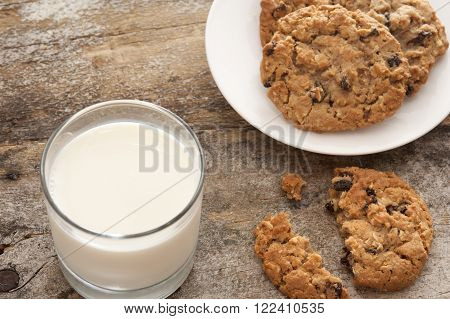 Milk and cookies in childhood tradition with a glass of farm fresh creamy milk and plate of choc chip cookies with one broken one on the old rustic wooden table