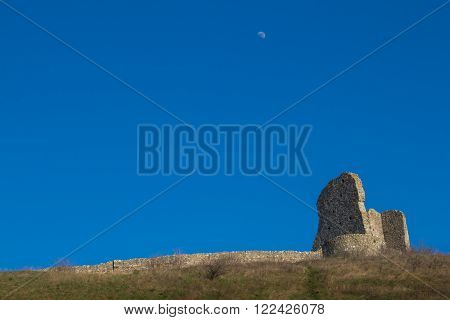 Part of the former fortress ruins of the Devin castle Bratislava Slovakia. Surrounding wall and a building on the hill. Bright blue sky with a moon.