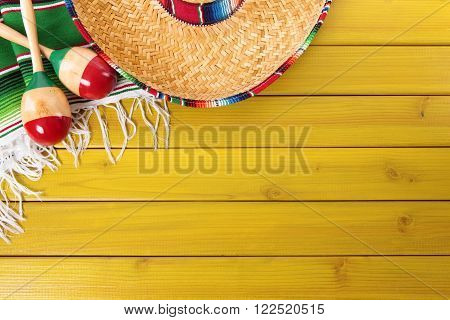 Mexican sombrero maracas and traditional serape blanket laid on a yellow painted pine wood floor. Space for copy.