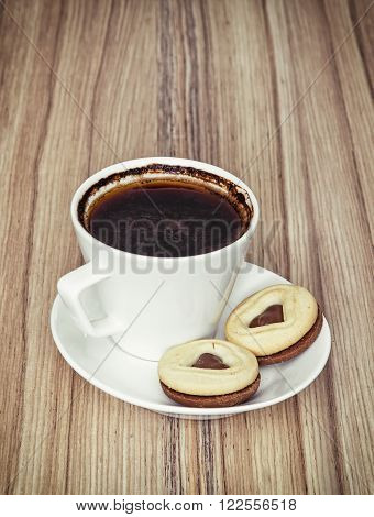 Cup of black coffee with two jam biscuits in the shape of heart on the wooden background.