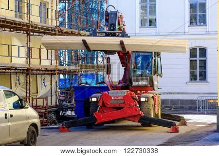 Kalmar Sweden - March 17 2016: A Manitou forklift with support legs out hold a bunch of planks next to some scaffoldings outside a building.