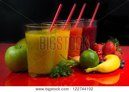 Colorful fresh pressed fruit green yellow oragne and red juices with fresh fruits and berries on black and red background
