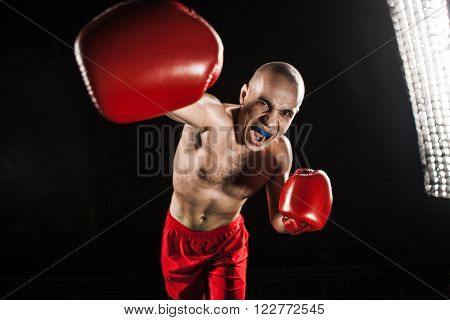 The young male athlete kickboxing on a black background  with kapa in mouth. concept fury in the fight
** Note: Shallow depth of field