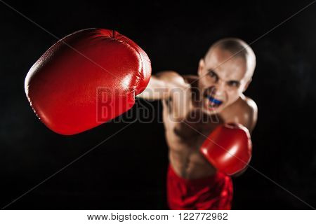 The young male athlete kickboxing on a black background with kapa in mouth. concept fury in the fight
** Note: Shallow depth of field