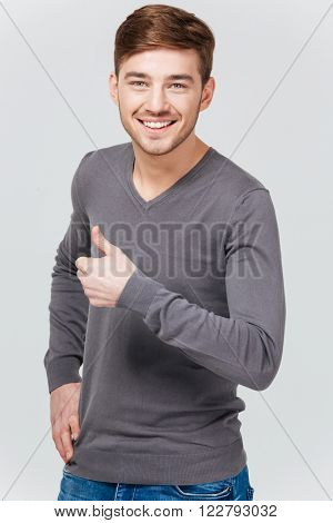 Happy handsome young man in grey pullover showing thumbs up over white background