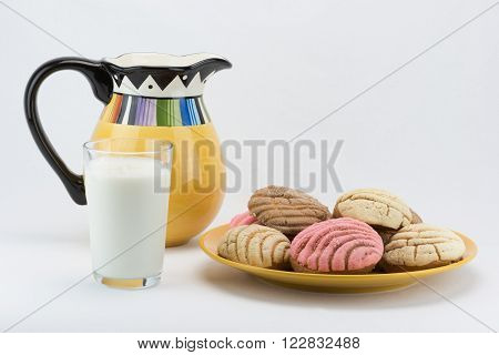 A glass of milk, a pitcher and a plate of concha bread.