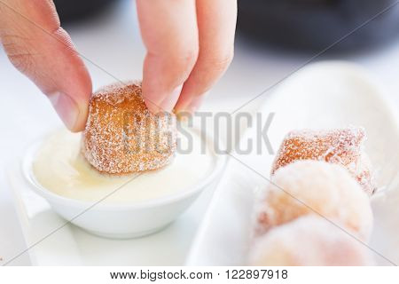 close-up of person's hand dipping fresh beignet in sauce traditional new orleans or french cuisine