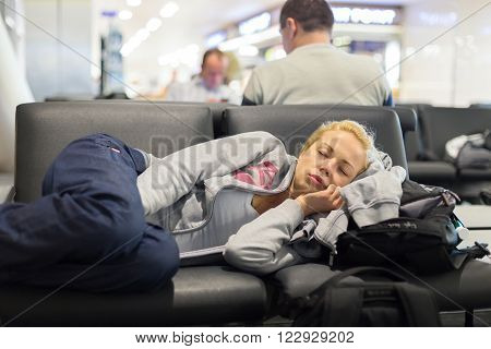 Tired female traveler sleeping on the airpot departure gates bench with all her luggage by her side.  Tireing travel concept.