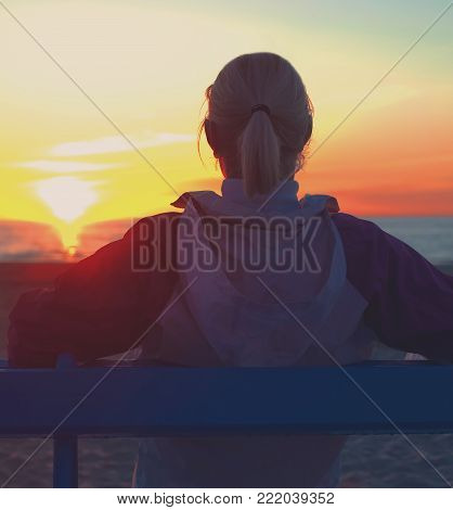 Girl sitting on a beach and looking on sinset