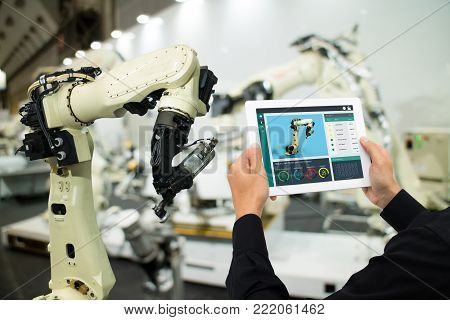 iot industry 4.0 concept,industrial engineer using software (augmented, virtual reality) in tablet to monitoring machine in real time.Smart factory use Automation robot arm in automotive manufacturing