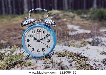 Vintage blue alarm clock on winter forest background. Daylight saving time concept winter time