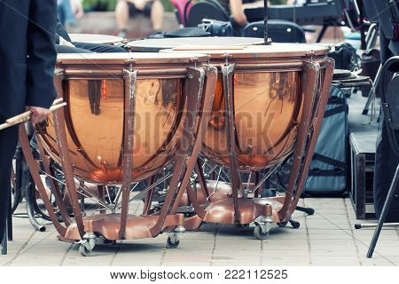 Timpani on stage. Timpani are musical instruments in the percussion family. A type of drum, they consist of a skin called a head stretched over a large bowl traditionally made of copper.