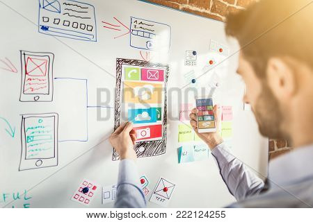 Designer man drawing website ux app development and holding smart phone on hand. User experience concept.