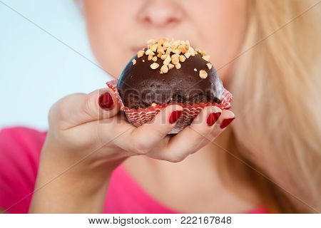 Diet, sweets, food concept. Woman holding delicious chocolate cupcake with peanut frosting about to take bite