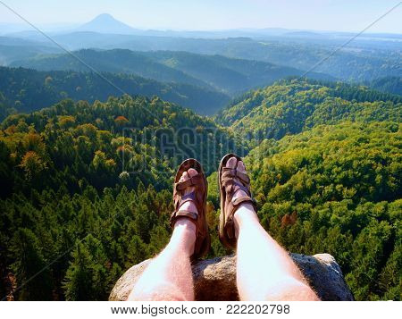 Long tired naked legs in hiking sandals on peak. Hiking in sandstone rocks, hilly landscape in blue misty cloud in background.