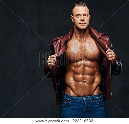 Studio portrait of shirtless muscular male dressed in a jeans and a leather jacket on naked torso over grey background.