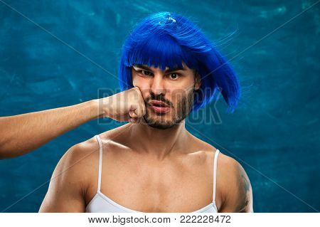 Unidentified male hand beating the face of pretty cross dressing man wearing blue wig and glasses