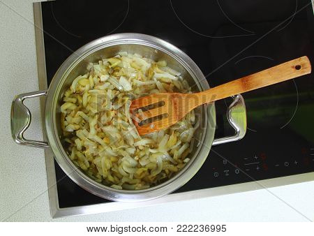 On the electric stove is a beautiful pan. In a frying pan at high temperature in vegetable oil delicious fried finely chopped onion.