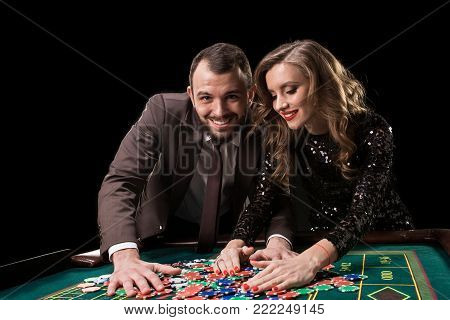 A man in a suit with a woman in a beautiful black dress playing roulette at the casino. Gambling. Casino. Roulette. Poker.