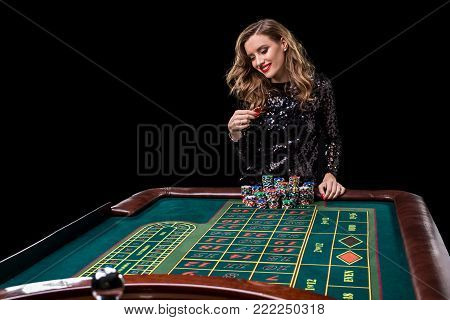 Sexy woman in a black dress playing in casino. Woman stakes piles of chips playing roulette at the casino club. Gambling. Roulette.