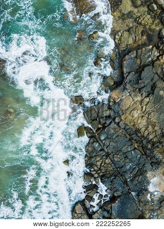 Lovely aerial beach drone photo of vibrant aqua waves crashing into rocks from the ocean.