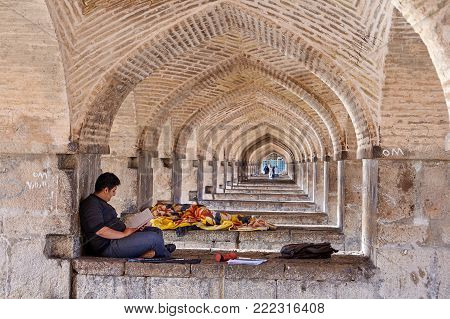 Isfahan, Iran - April 24, 2017: A young man reads notes in a notebook, lying on a stone in a vaulted arched corridor under a Khaju bridge.