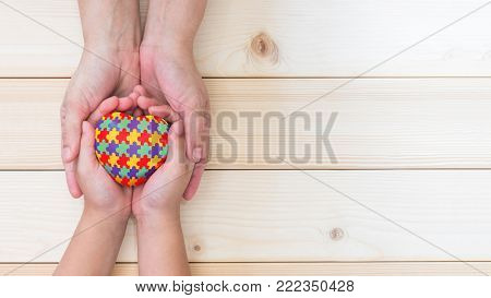 World Autism Awareness day concept with puzzle or jigsaw pattern on heart with autistic child's hands supported by nursing family caregiver