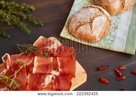 Fresh green thyme and hot red pepper. Succulend bacon on a wooden board. Freshly baked hand-made bread on a kitchen towel.