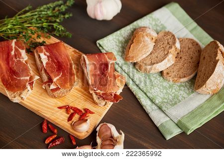 Sandwiches made from hand-made rye bread and thin chopped fresh bacon. Succulend bacon on a wooden board. Fresh green thyme and hot red pepper.