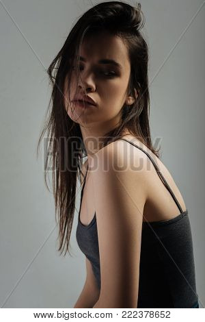 Beautiful. Attractive preoccupied dark-haired young woman thinking and looking down and wearing a top