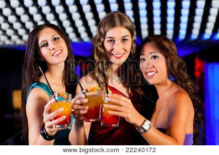 Group of party people - three friends - with cocktails in a bar or club having fun