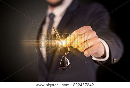 Businessman hand  over shiny keys in dark suit with dark background