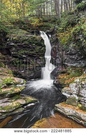 Adams Falls, one of many beautiful waterfalls in Pennsylvania's Ricketts Glen State Park, splashes through a rocky ravine in autumn.