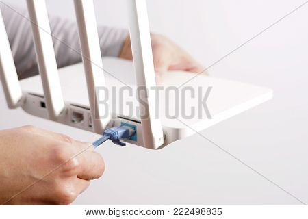 The back view of router showing the lan internet port, and the hand is pluging in the land cable on a white router